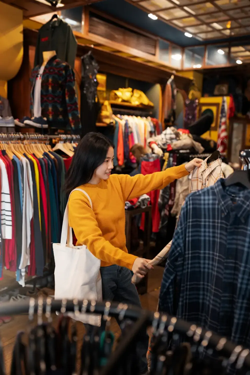Woman shopping for clothing and browsing shirts on racks inside a fashion retail store.